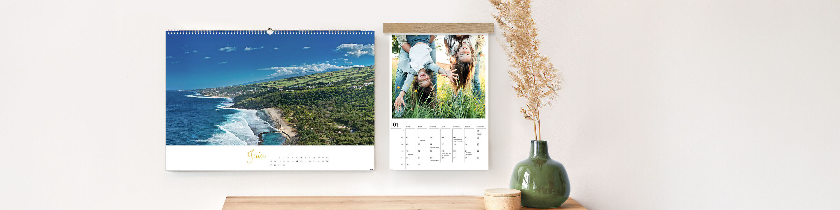 Deux calendriers photo CEWE sont accrochés au mur. L'un montre un paysage avec mer et montagnes, l'autre un groupe de personnes dans la nature.
