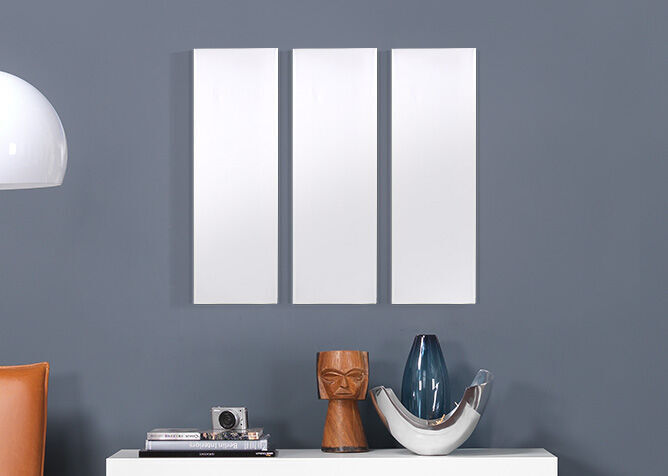Trois cadres blancs vides sur un mur gris au-dessus d'un buffet avec des objets décoratifs.
