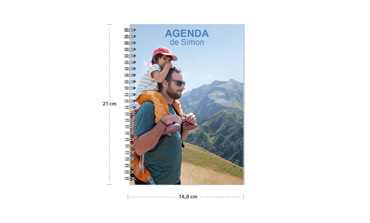 Un carnet coloré sur une montagne avec une personne portant un sac à dos d'enfant. Sur la couverture, il est écrit 'AGENDA de Simon'