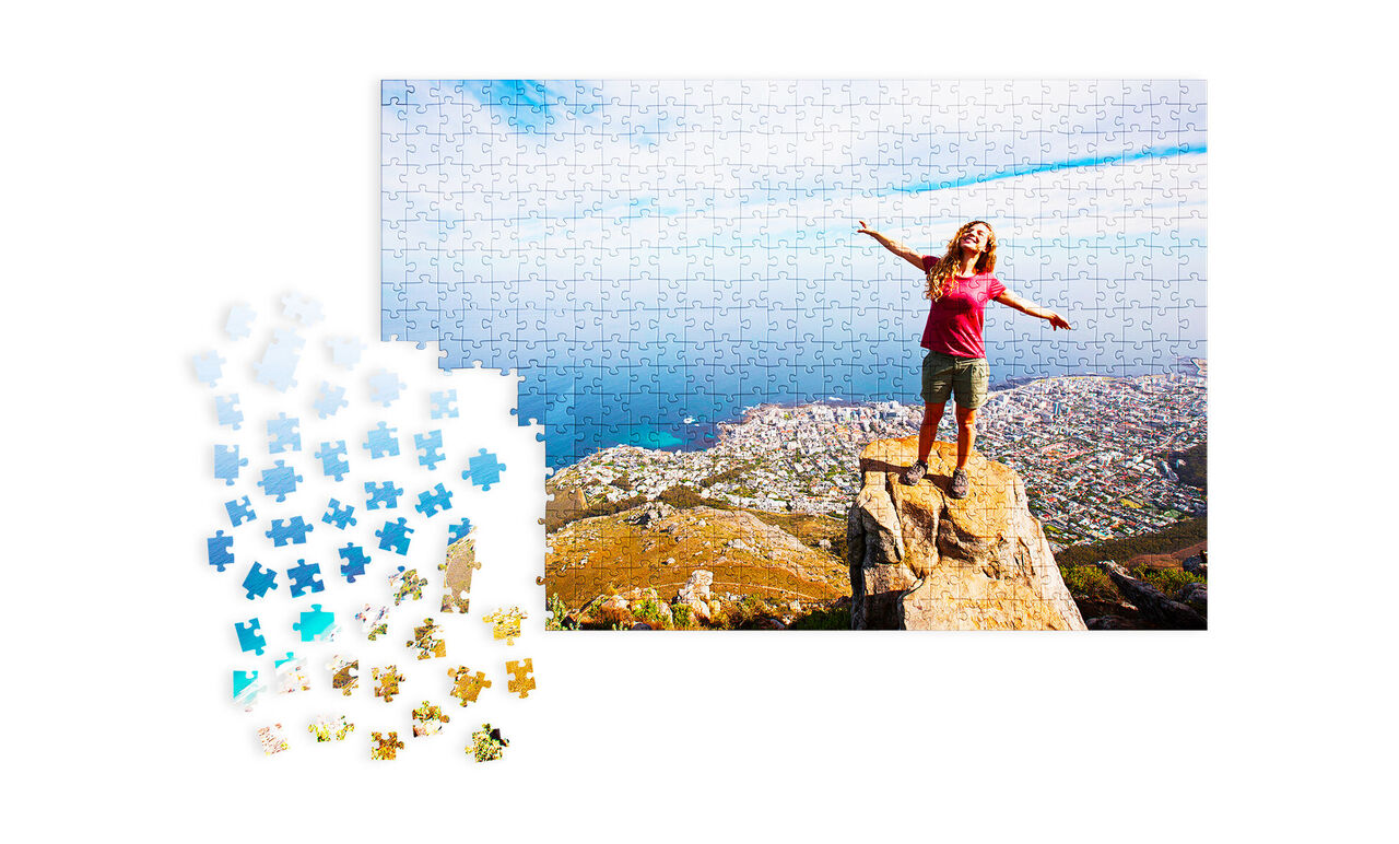 Une femme heureuse se tient sur un rocher les bras largement ouverts. En arrière-plan, un beau paysage de montagnes et de mer. Des morceaux de puzzle colorés sont visibles.