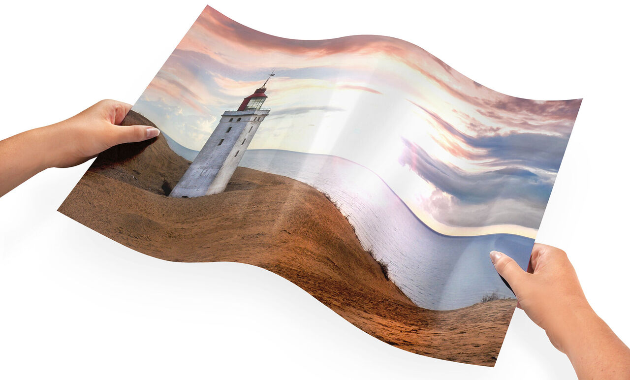 Une personne tenant une affiche délicatement empilée d'un phare sur la plage. Le coucher de soleil colore doucement le ciel.