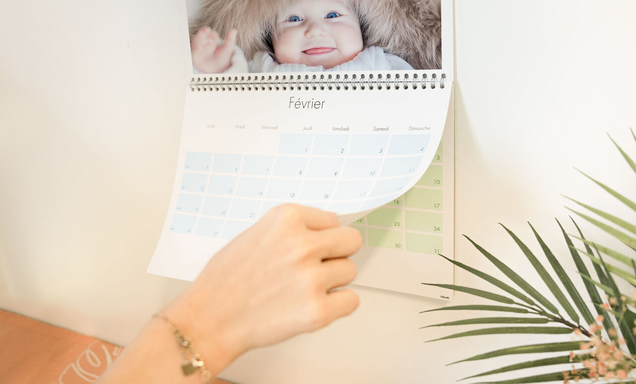 Une main feuillette un calendrier avec aperçu mensuel et cases colorées.