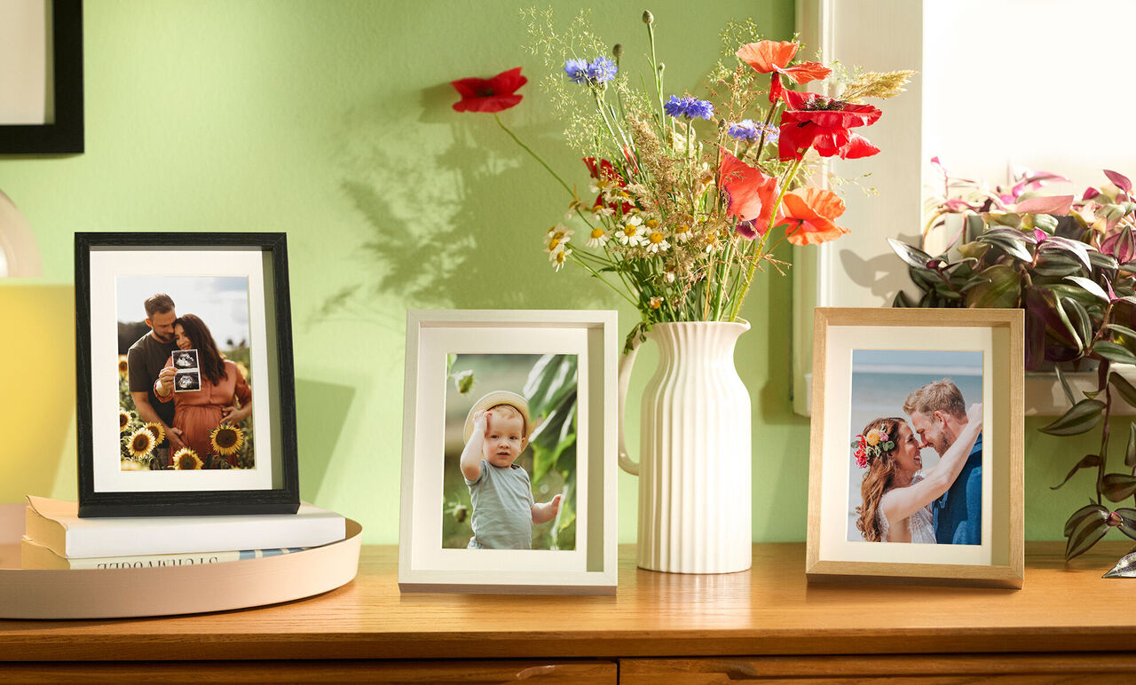 Trois cadres photo avec de belles photographies sur une commode entourée de fleurs.