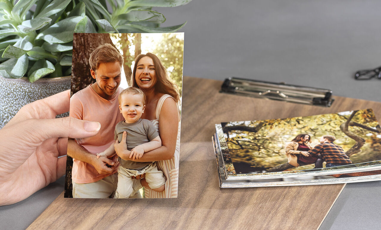 Une personne tient une carte photo avec une famille dans la nature. Un livre photo et une plante sont en arrière-plan