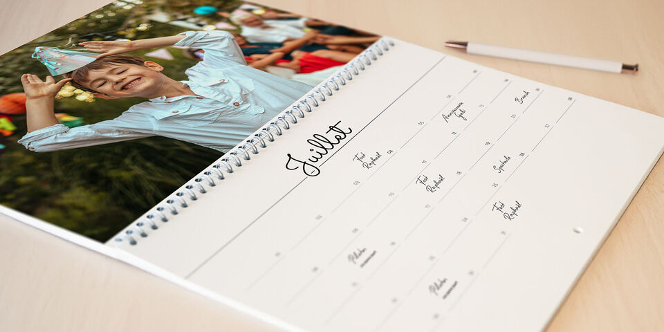 Un enfant joyeux avec un chapeau de fête sourit dans le mois de juillet d'un calendrier photo CEWE.