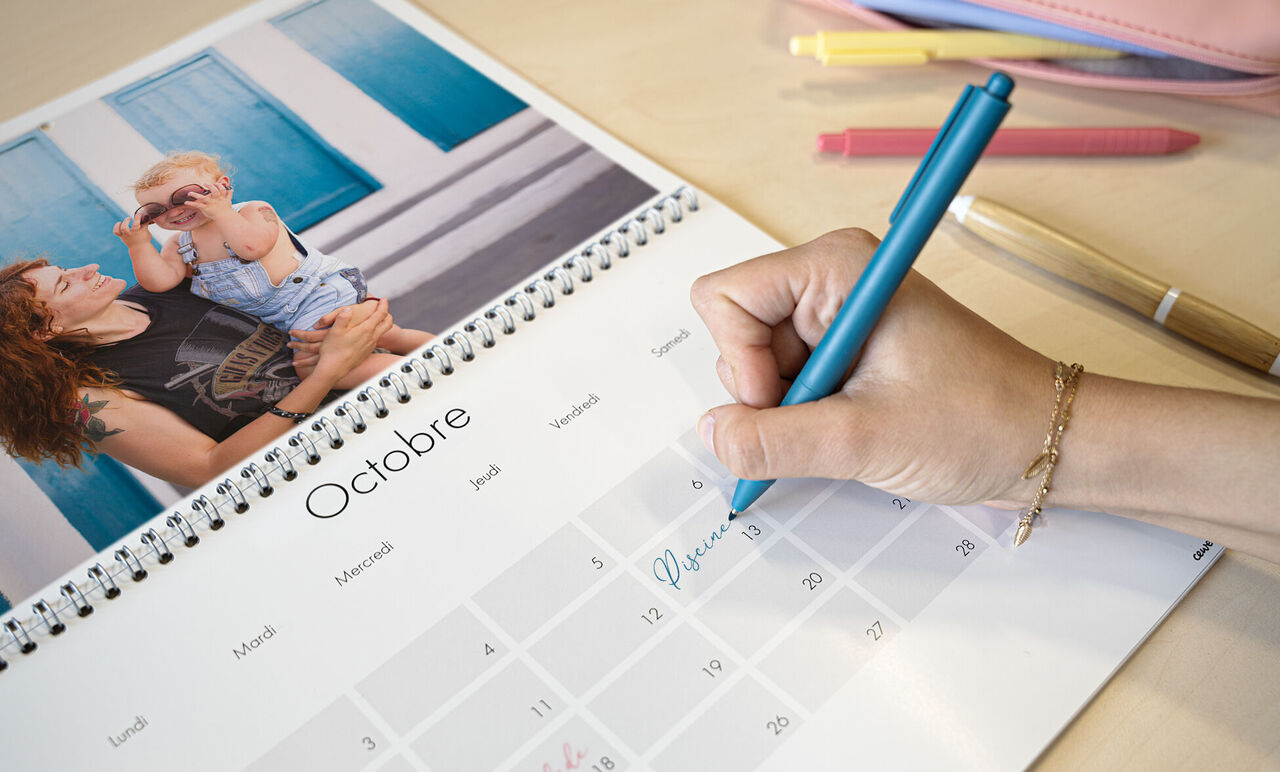 Une personne écrit dans un calendrier photo tout en tenant un enfant dans ses bras. Le calendrier montre octobre.