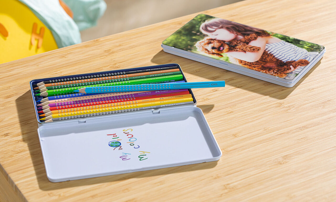 Crayons de couleur dans une boîte avec une photo d’un enfant et d’un chien en arrière-plan.
