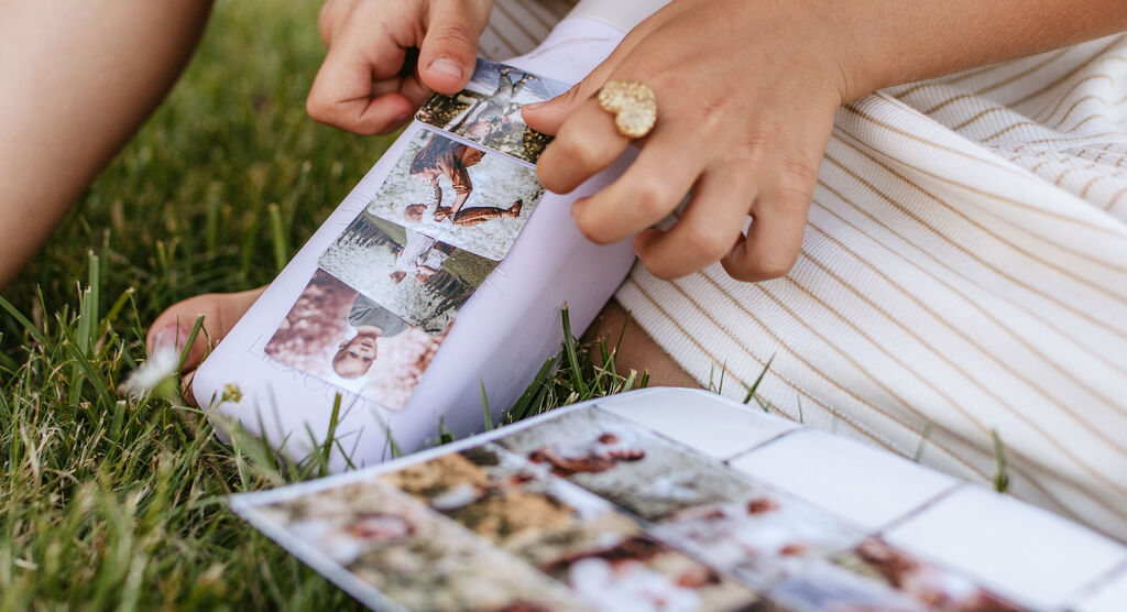 Une personne consulte des photos dans un album CEWE, tenant une autre image, entourée d'herbe verte.
