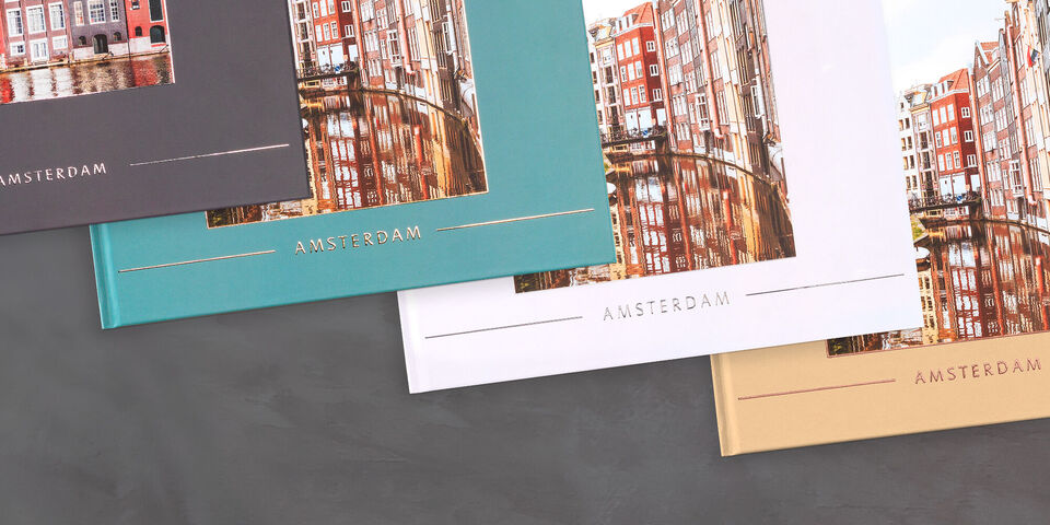 Trois livres photo CEWE de différentes couleurs avec une image de l'architecture d'Amsterdam sur la couverture.