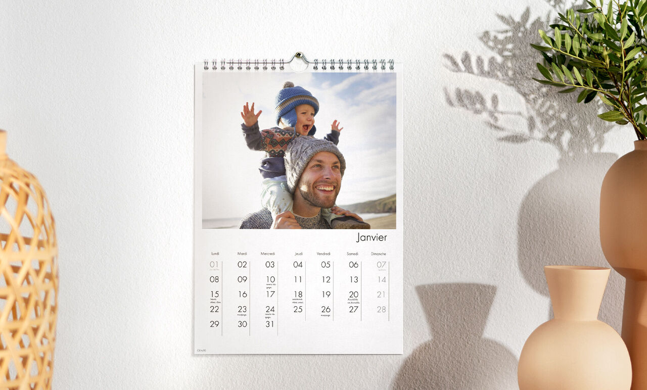 Un calendrier mural montre un enfant joyeux assis sur le dos d'un adulte en train de célébrer. Le calendrier affiche janvier.