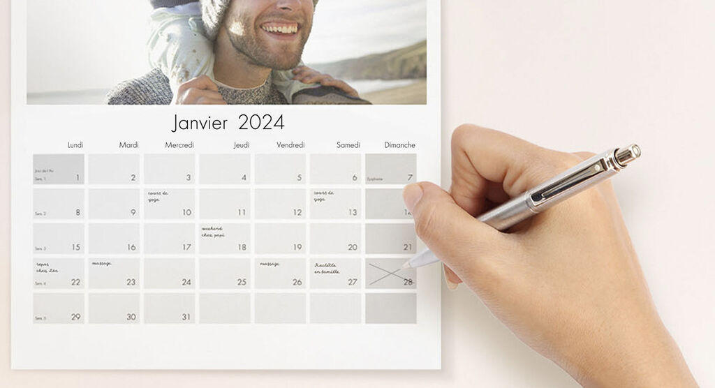 Une main avec un stylo modifiant un calendrier de janvier 2024 avec des cases claires.