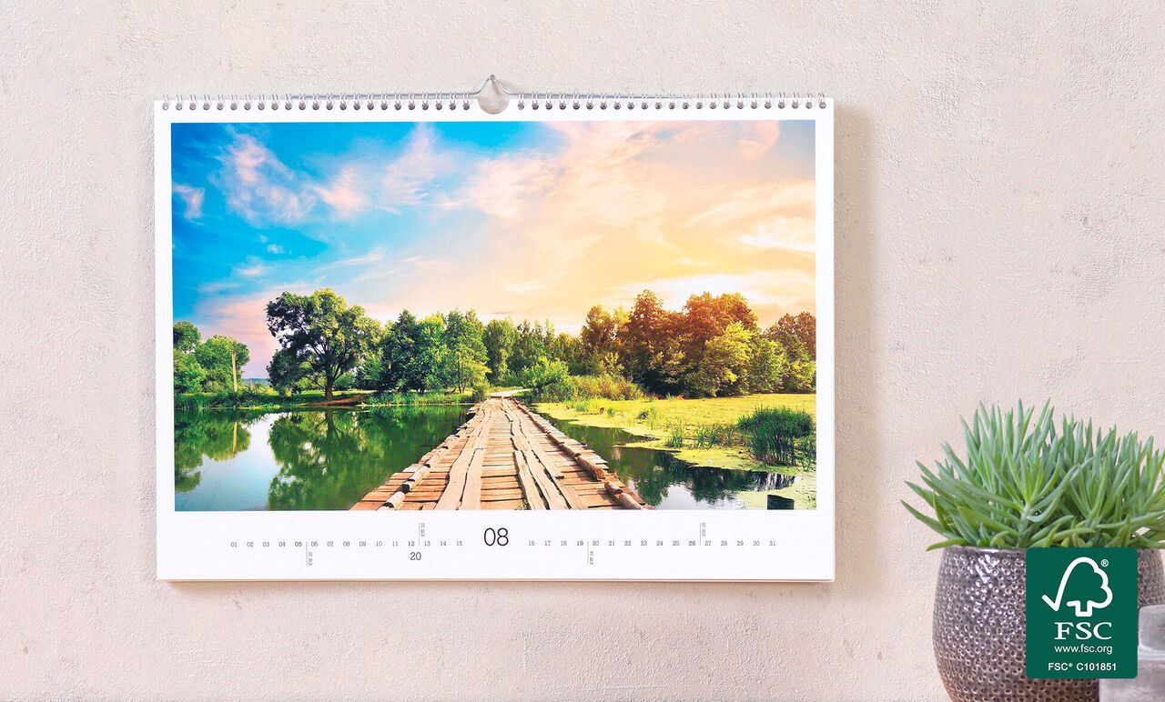 Un magnifique calendrier photo montrant un paysage paisible avec un chemin en bois sur un lac, entouré d'arbres et de champs.