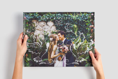 Le couple de mariés tient un CEWE PhotoBook floral dans ses mains.