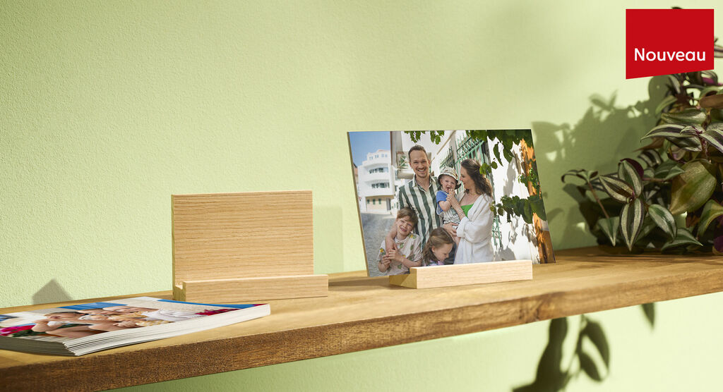Une famille pose joyeusement devant un fond vert, entouree de plantes. Un livre photo et un cadre sont sur une étagère en bois.