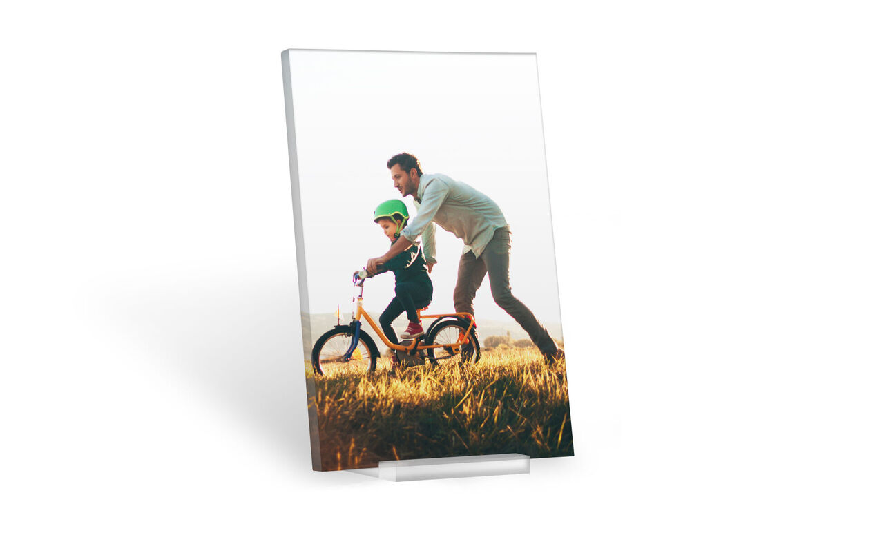 Un père joyeux pousse son fils sur un vélo coloré à travers un champ ensoleillé. Les deux portent des casques et profitent du moment ensemble.