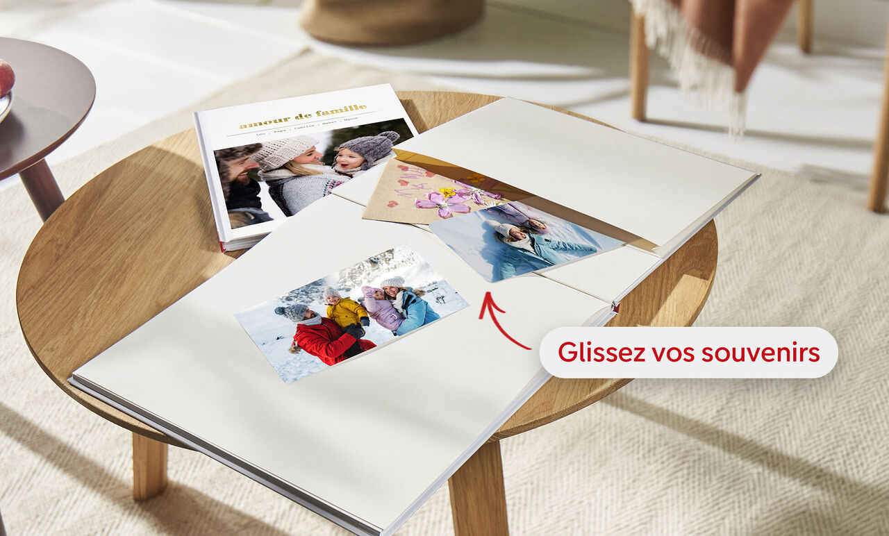 Un livre photo ouvert sur une table en bois montre des souvenirs personnels. Une main tient une photo sur une page.