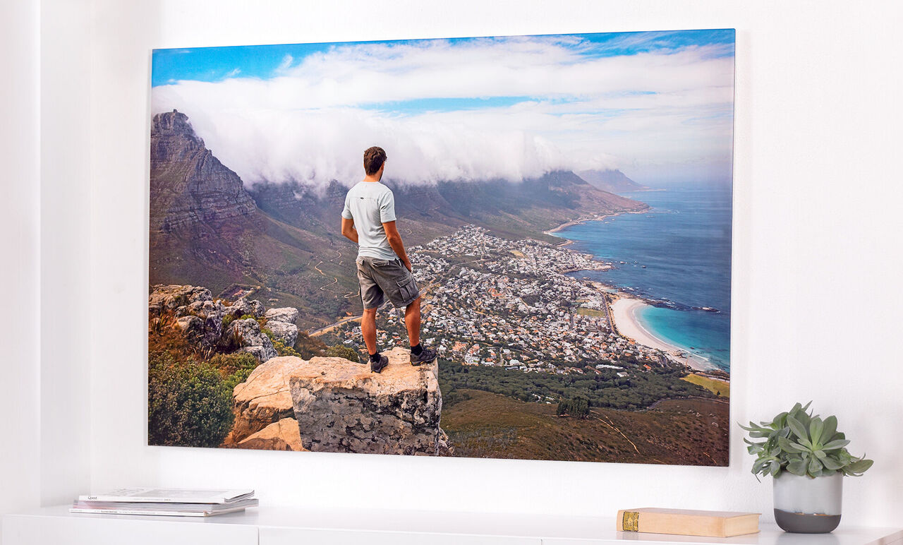 Un homme se tient sur un promontoire et regarde un paysage côtier avec ville et montagnes.