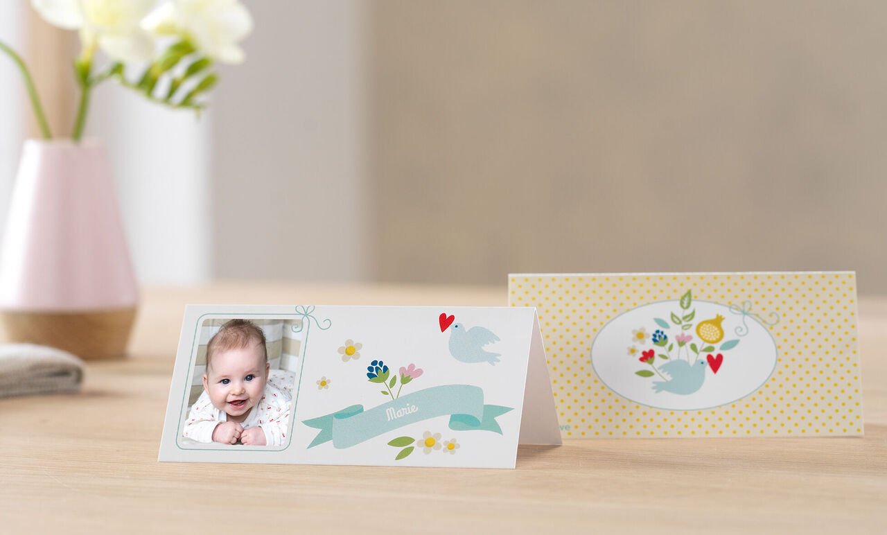 Deux cartes de voeux soigneusement conçues sur une table, l'une avec une image et motifs floraux, l'autre à pois jaunes avec motifs d'oiseaux. CEWE Cartes