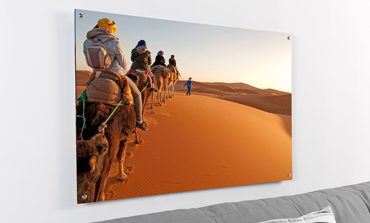 Un groupe de personnes monte des chameaux à travers un paysage désertique ensoleillé. Les dunes brillent en orange.
