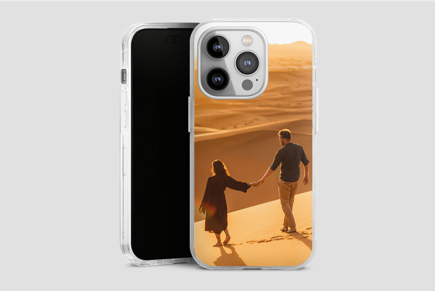Un couple se tient par la main en marchant dans une dune de sable doré au coucher du soleil.