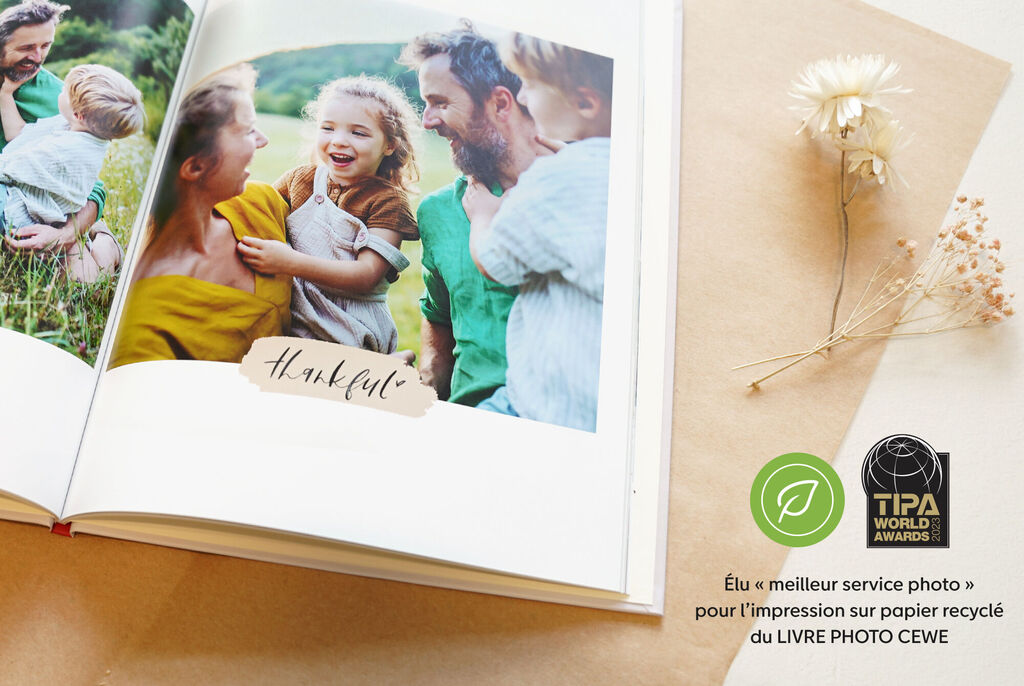 Un livre photo avec des souvenirs de vacances sur une belle surface, entouré d'un chapeau de paille et d'une fleur. CEWE PHOTOBOOK