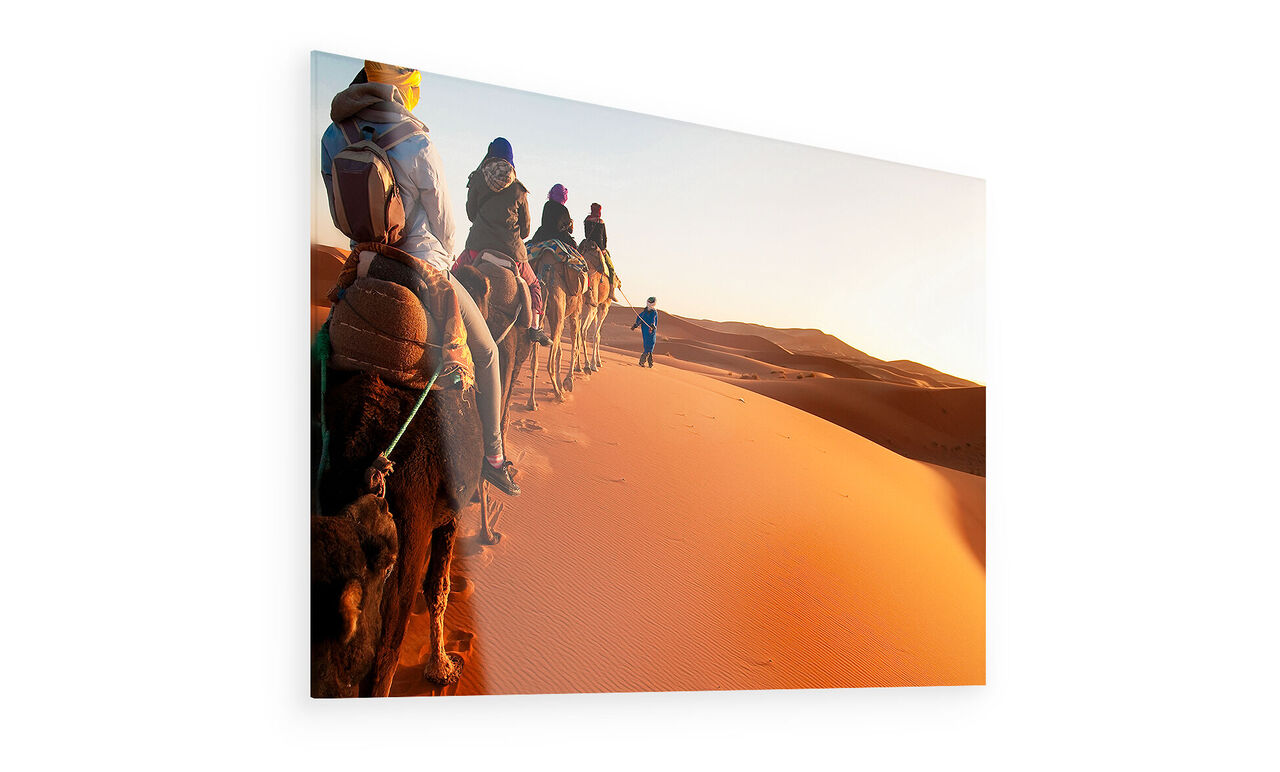 Six personnes montent sur des chameaux à travers les dunes du désert au coucher de soleil.