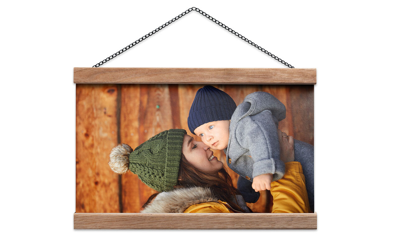 Une mère souriante tient son bébé en vêtements chauds devant un mur en bois.