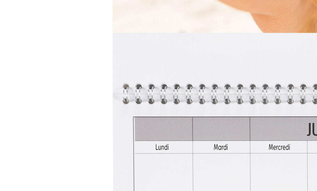 Sur une table se trouve un calendrier photo CEWE. Le mois de juin est visible sur la page ouverte avec les jours listés, design moderne.