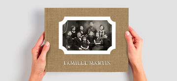 Deux mains tiennent un album photo CEWE avec une photo de famille et le titre "Famille Martin".