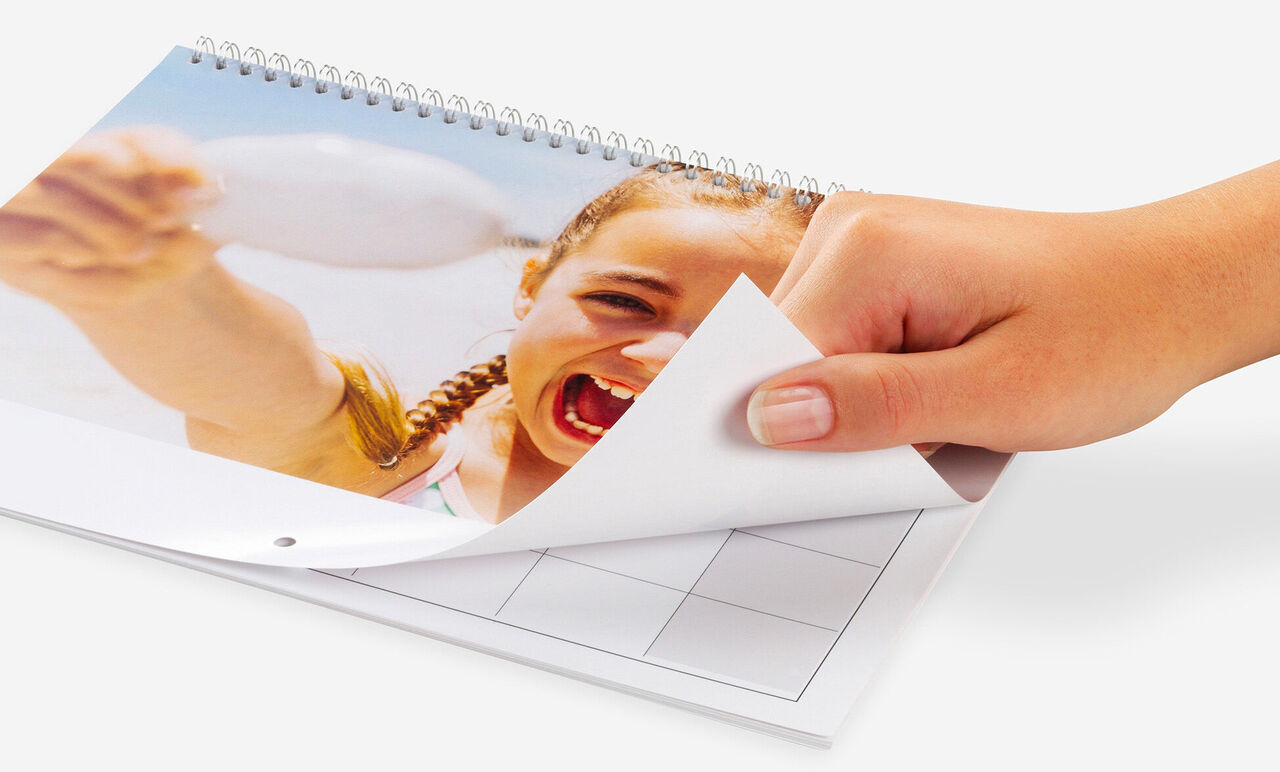 Des mains feuillettent un calendrier photo CEWE avec un motif joyeux.