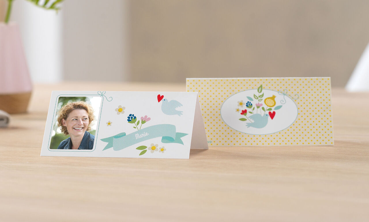 Deux cartes de vœux CEWE joliment conçues sur une table, l'une avec une photo et des motifs floraux